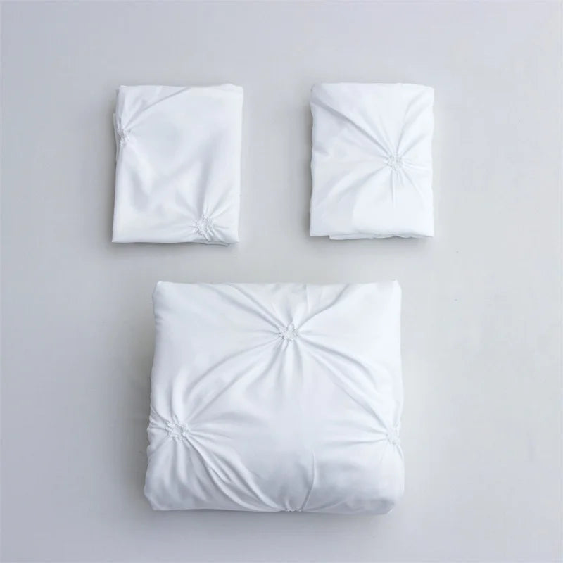 Three white queen comfort bedding items including two pillowcases and one comforter laid out on a light gray surface