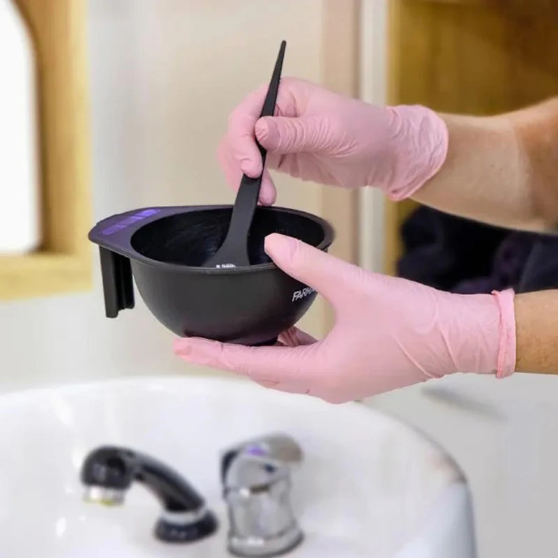Hands in pink nitrile gloves are holding a black cooking pot over a sink for cleaning tasks.