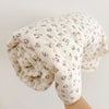 A rolled floral muslin baby blanket in off-white with red and blue floral patterns.