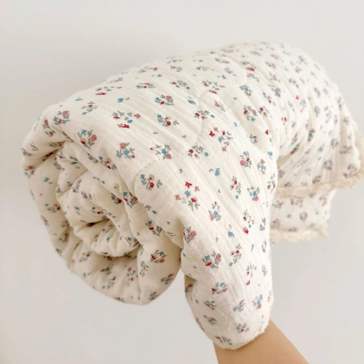 A rolled floral muslin baby blanket in off-white with red and blue floral patterns.