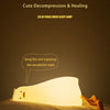 A white silicone duck night light is lying on a bed, illuminating the surrounding area.