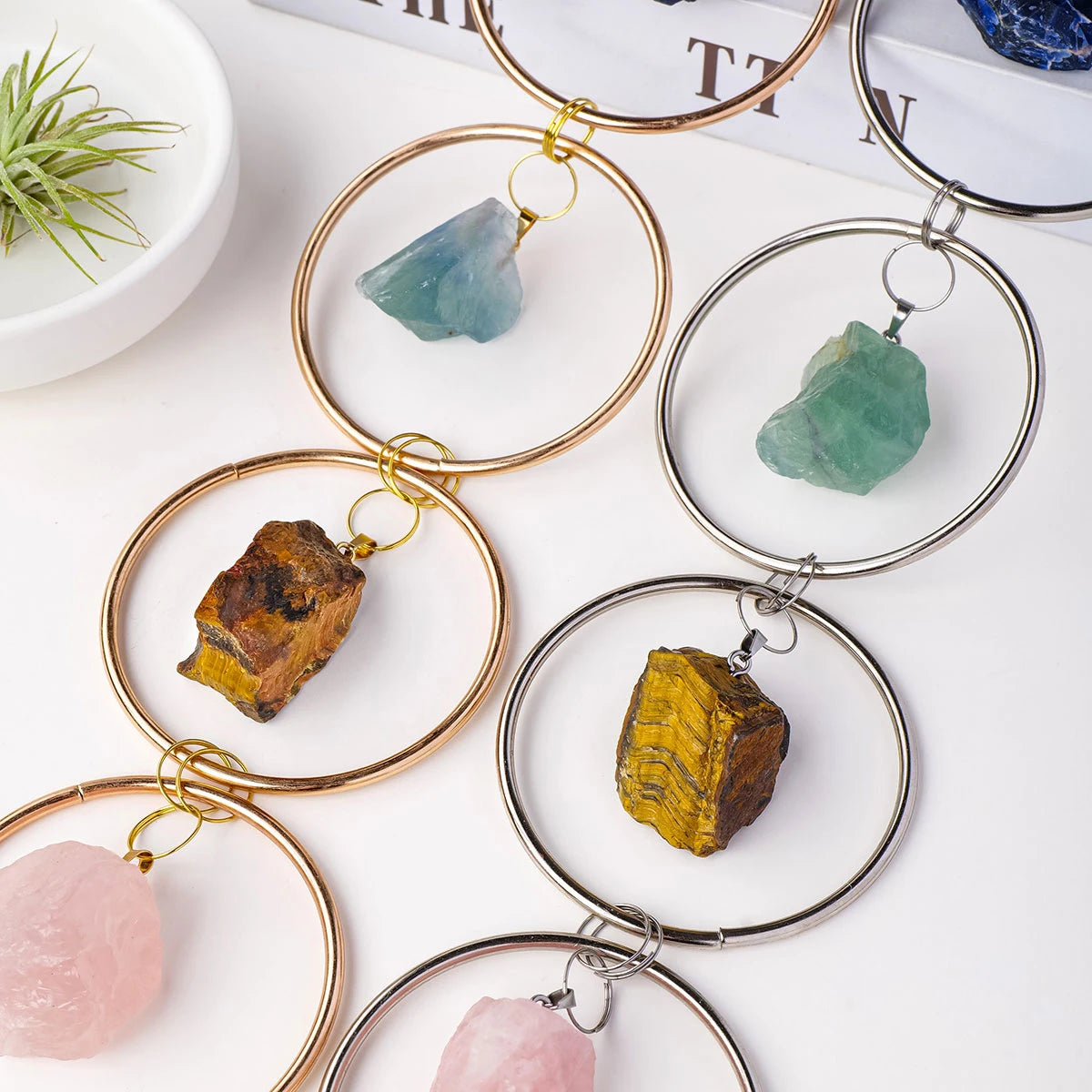 Gold-toned crystal hanging decor featuring various natural stones and green plant in a white bowl