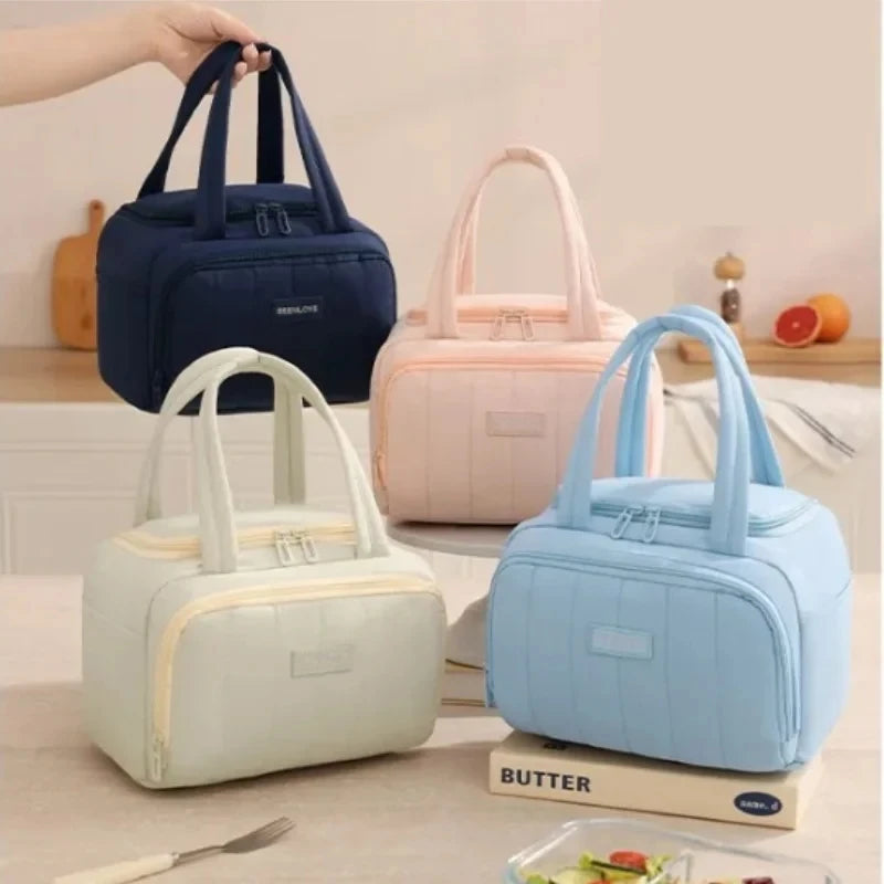 Three pastel-colored insulated quilted lunch tote bags in blue, pink, and mint green are displayed on a light wooden surface.