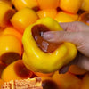 Eine Hand drückt einen leuchtend gelben, glatten Stressball mit orangefarbener Karamellfüllung.