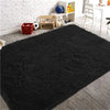 A dark gray luxury velvet plush carpet placed on a wooden floor with decorative items and a white chair in the background.