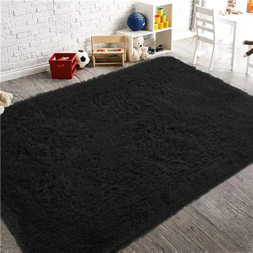 A dark gray luxury velvet plush carpet placed on a wooden floor with decorative items and a white chair in the background.