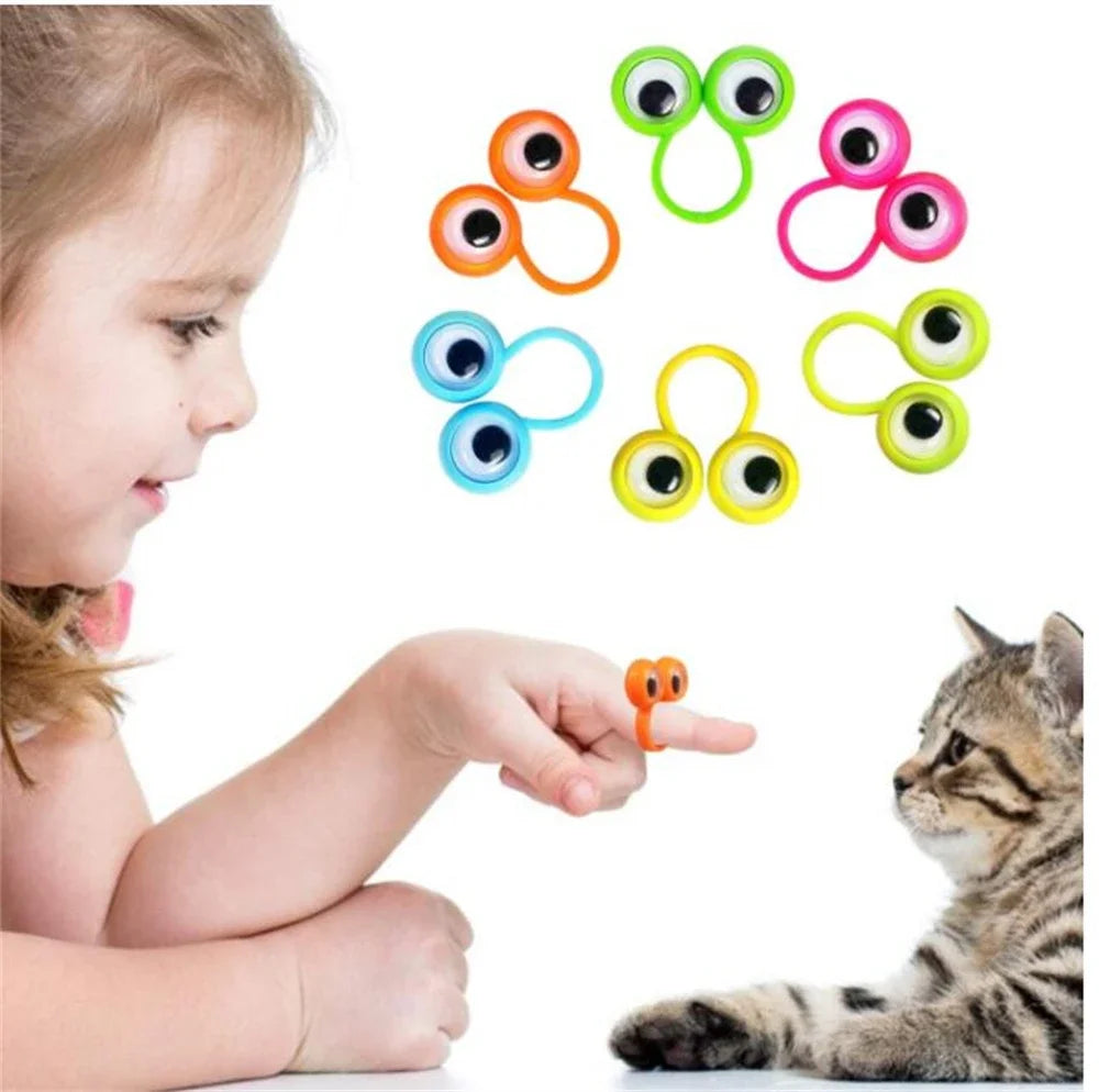 A child's finger is interacting with a set of colorful eye-shaped finger puppet rings for a party favor.
