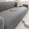 A gray plush sofa cover with a light beige throw pillow and a small wooden dish on the surface.