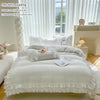 A white ruffled duvet cover set displayed on a bed with pillows and accessories near a window.