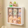 A white wall-mounted display case holds three fluffy, animal-like collectible dolls in various pastel colors.