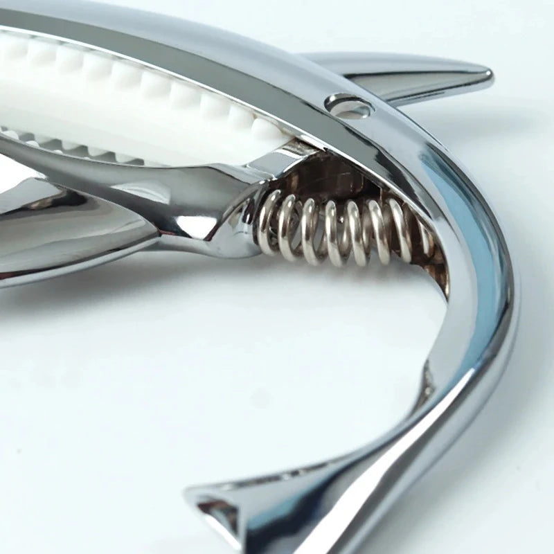 A close-up view of a silver guitar capo with a zinc alloy build and a visible tuning mechanism.