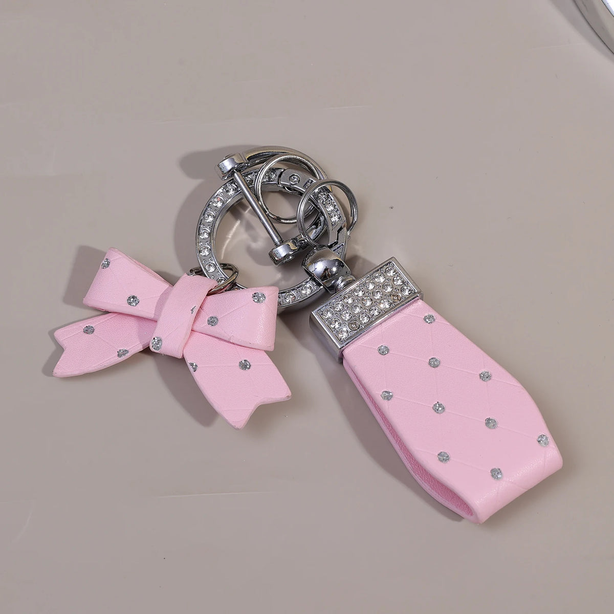 Pink PU leather bow keychain with an O-shaped silver buckle and rhinestone accents