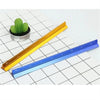 A precision aluminum triangular scale ruler is shown next to a potted cactus on a grid background.