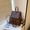 Mini sac à dos en cuir marron avec cordon, posé sur une boîte blanche.