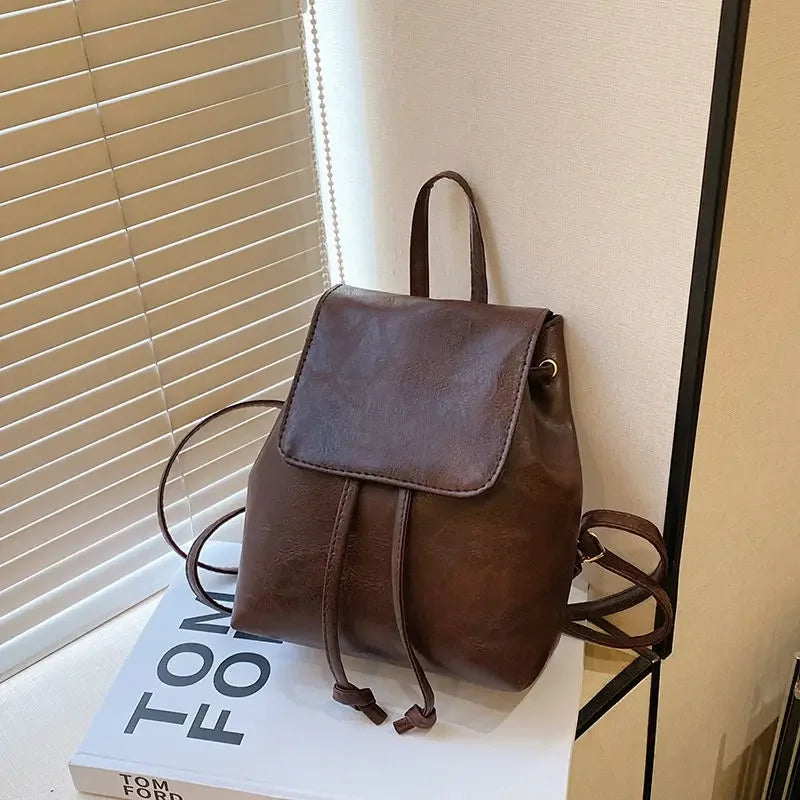 Mini sac à dos en cuir marron avec cordon, posé sur une boîte blanche.