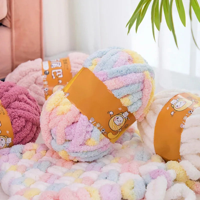 A pile of fluffy, multicolored chenille yarn in pinks, yellows, and blues is displayed on a white surface.