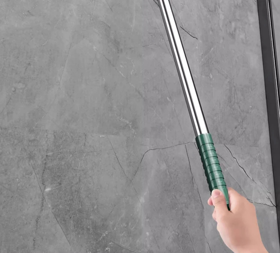 A hand is holding a long, silver silicone scraper broom and squeegee against a gray stone surface.