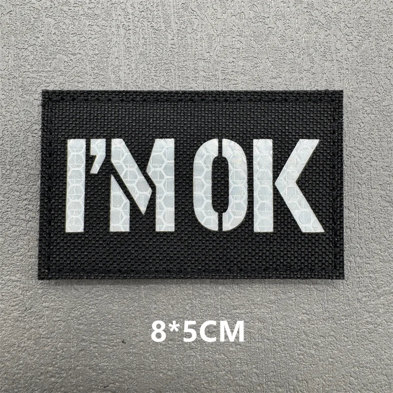 Black embroidered patch with white text I'M OK on a gray background