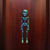 A small, green, poseable skull figure displayed against a dark wooden background.