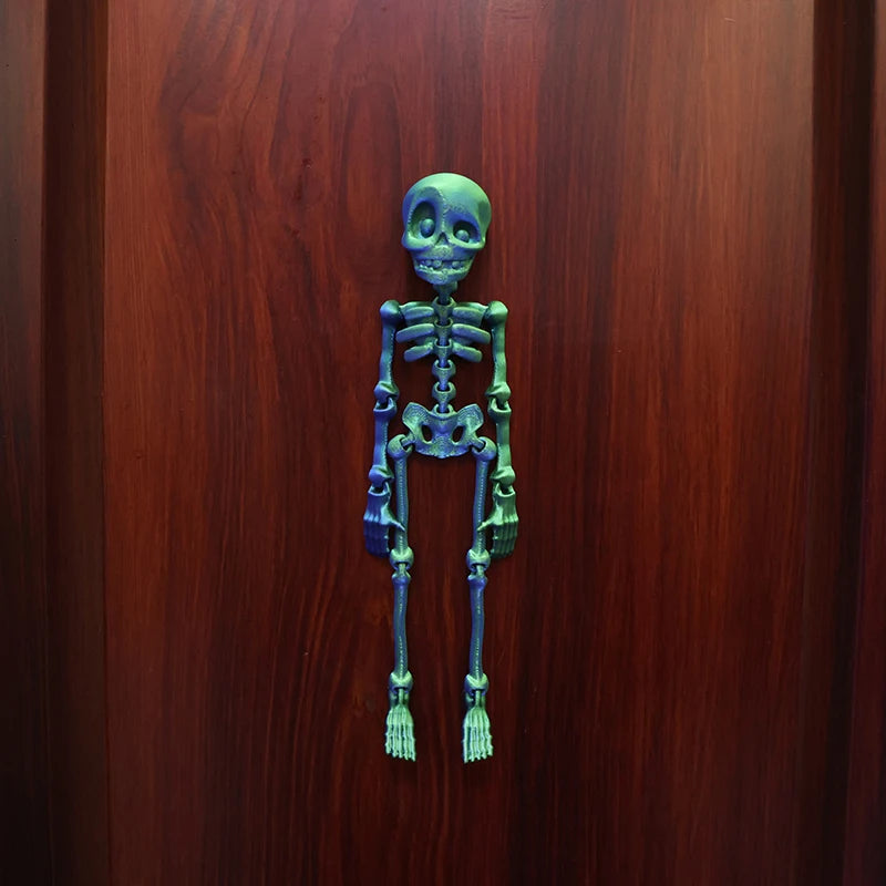 A small, green, poseable skull figure displayed against a dark wooden background.