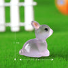 A small, translucent pink resin bunny figurine sitting on green grass.