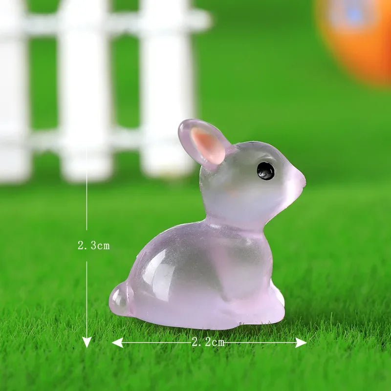 A small, translucent pink resin bunny figurine sitting on green grass.