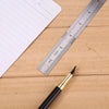A stainless steel precision ruler is shown next to a piece of paper on a wooden surface.
