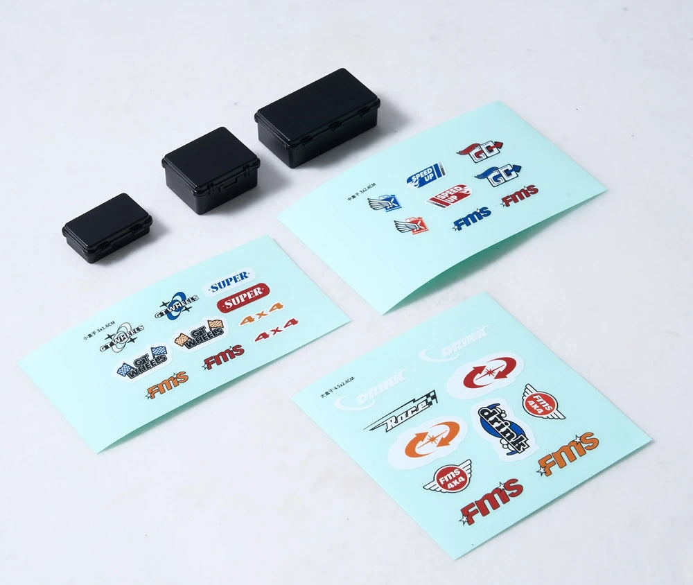 A set of black RC car decorative accessories including a surfboard, kayak, and roadblocks displayed on a white surface.