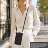 A woman wearing a white shirt and pants holds a black compact PU leather crossbody bag.