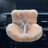 A fluffy peach colored miniature doll seat car vent decoration installed in a car's air vent.