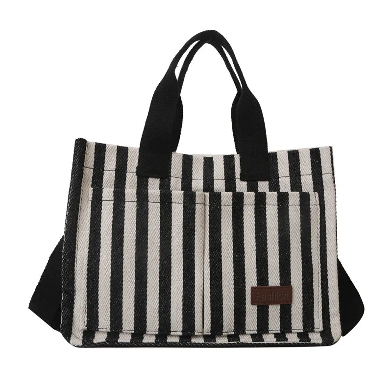 A black and white striped canvas tote bag with black handles and inner pockets.