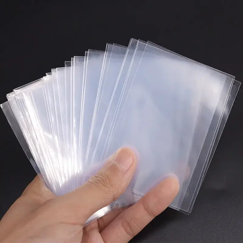A hand holds a stack of clear plastic card sleeves for collectible cards.