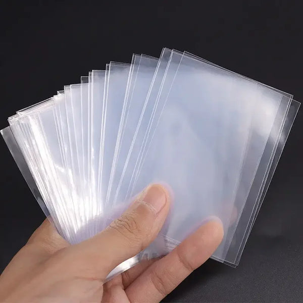 A hand holds a stack of clear plastic card sleeves for collectible cards.