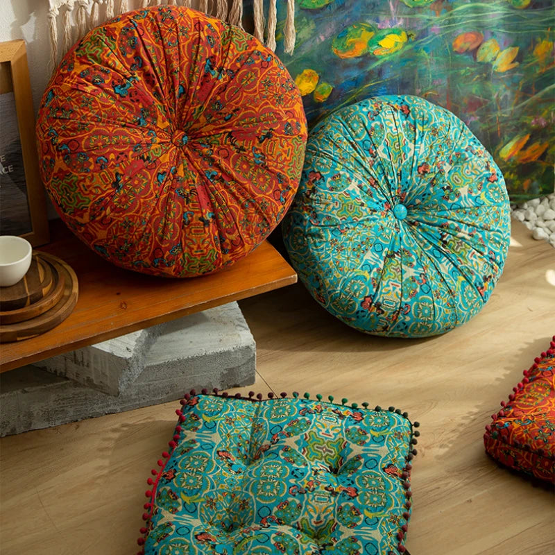 A vibrant orange and green patterned floor cushion sits on a wooden shelf next to a blue and teal patterned cushion.