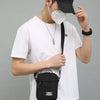 A person wearing a white t-shirt and black cap holds a black mini crossbody phone bag.