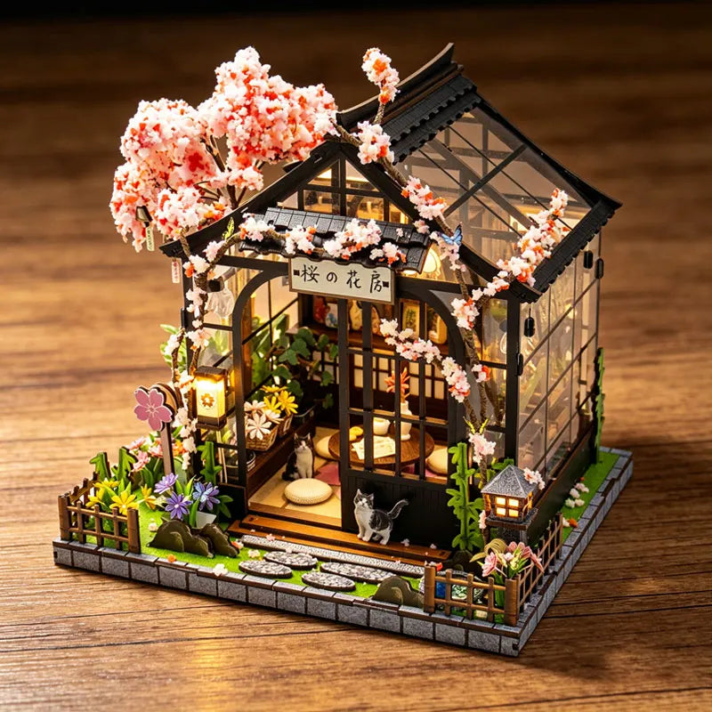 A detailed miniature Japanese sakura tea house model featuring pink blossoms, greenery, and a wooden structure.