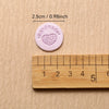 A round pink handmade label is shown next to a wooden ruler for scale.
