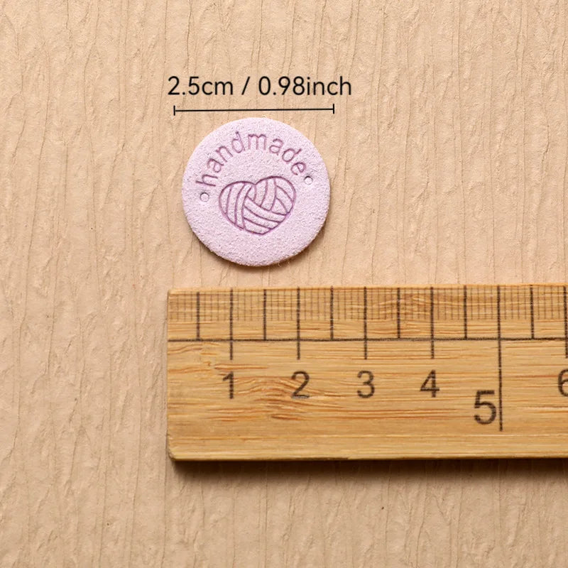 A round pink handmade label is shown next to a wooden ruler for scale.