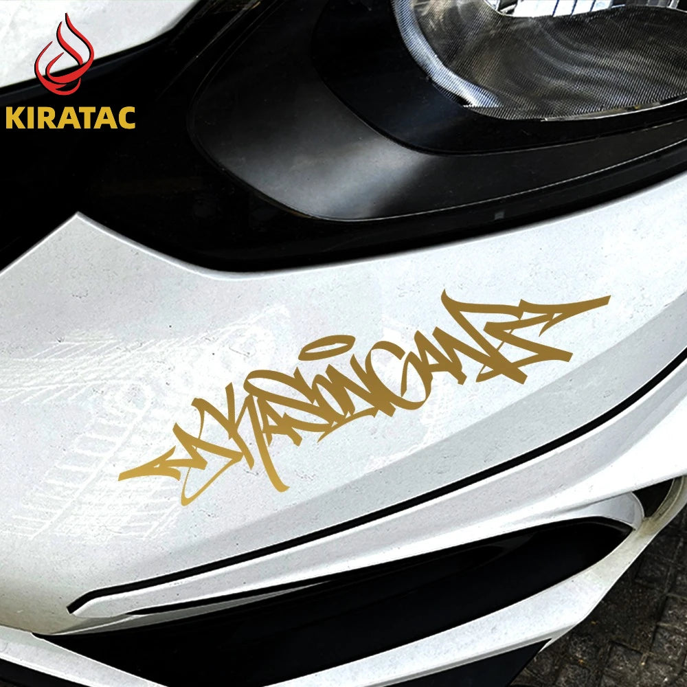 A close-up of a white motorcycle helmet featuring a gold wildstyle graffiti decal on the front panel.