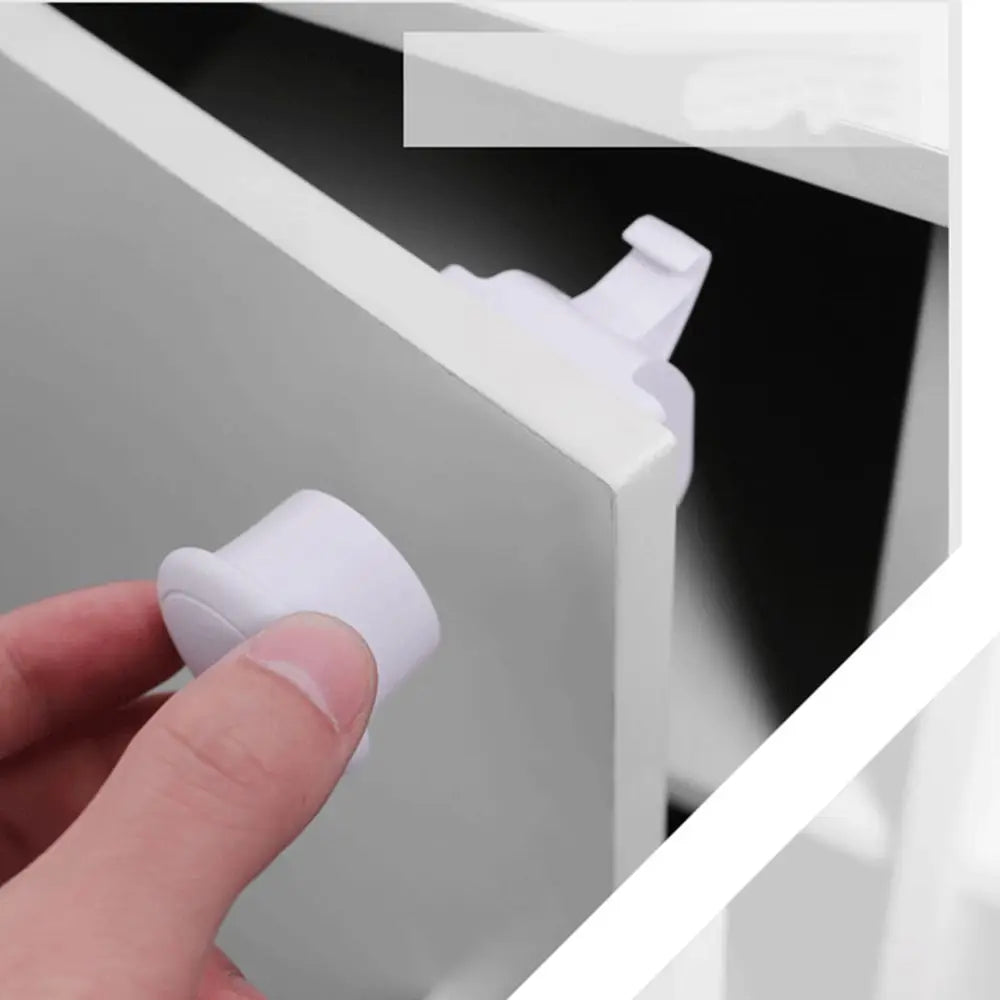 A hand is operating a white magnetic cabinet lock for baby safety on a drawer or cabinet.