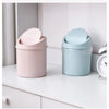 A pink compact covered desktop trash bin with a light blue flip lid sitting on a white surface.