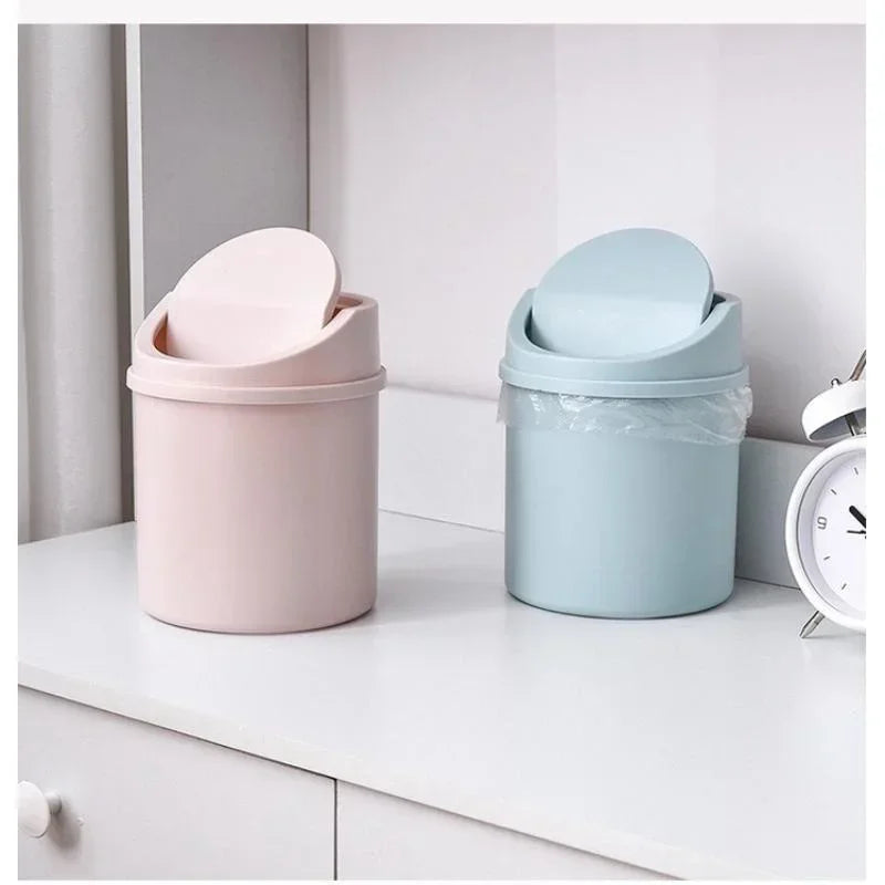 A pink compact covered desktop trash bin with a light blue flip lid sitting on a white surface.