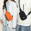 A woman is shown wearing a white jacket and blue jeans, carrying an orange water-resistant nylon chest sling bag.