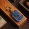 A dark blue leather key fob is resting in a wooden box, next to a brass keyring.