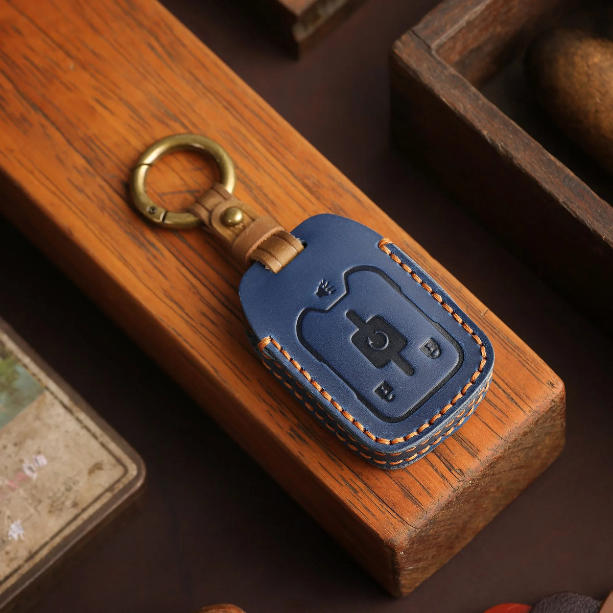 A dark blue leather key fob is resting in a wooden box, next to a brass keyring.