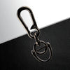 A silver metal key ring with a clasp and a circular loop is displayed on a black leather surface.