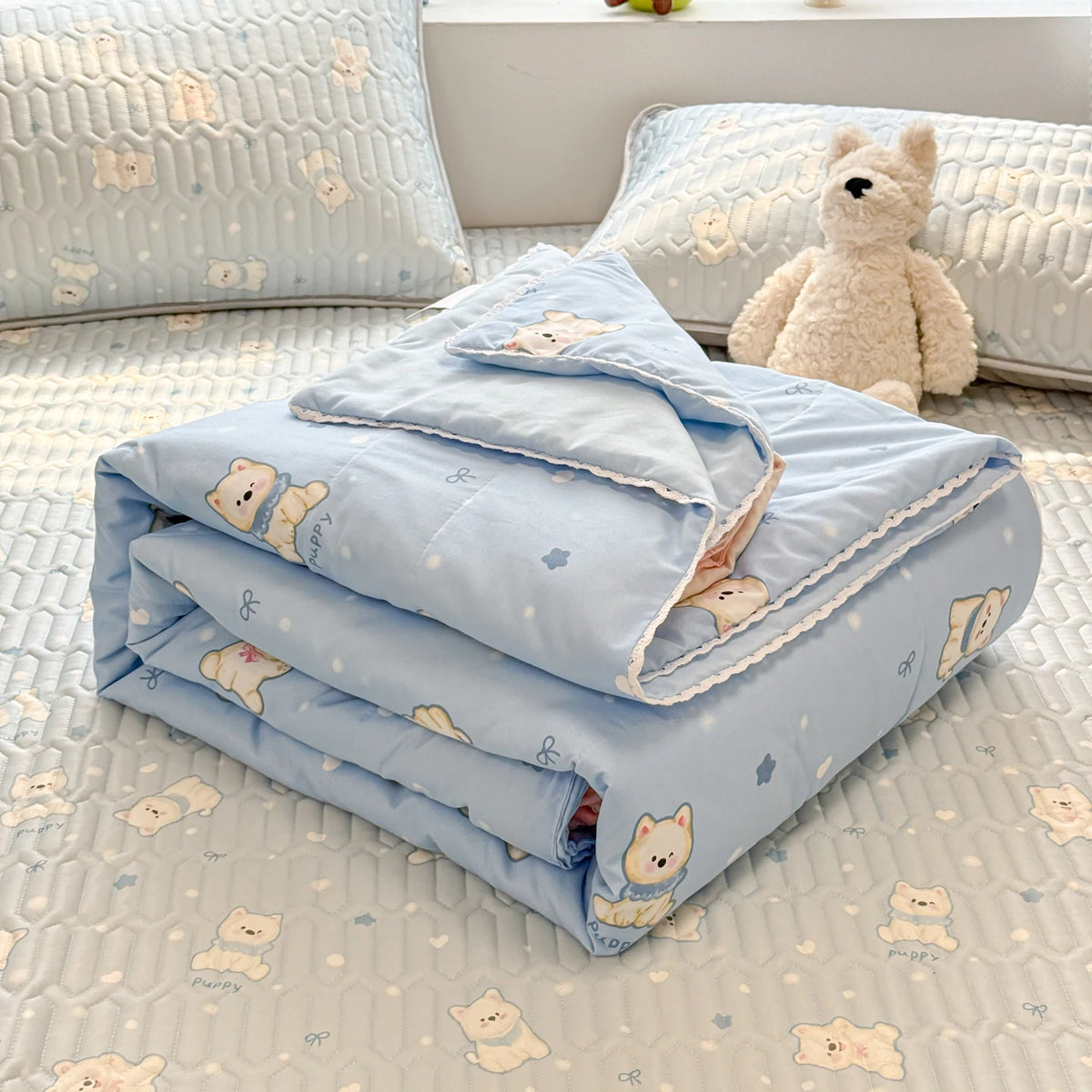 Light blue lace-trimmed breathable summer duvet folded on a white textured surface with a teddy bear.