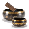 A handcrafted Tibetan singing bowl with a wooden cushion and striker, shown in profile.