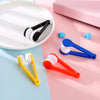 A collection of portable double-sided glasses cleaning brushes in black, white, blue, and orange resting on a pink surface.