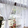 Rideau transparent avec broderie florale blanche, suspendu à une fenêtre avec vue floue extérieure